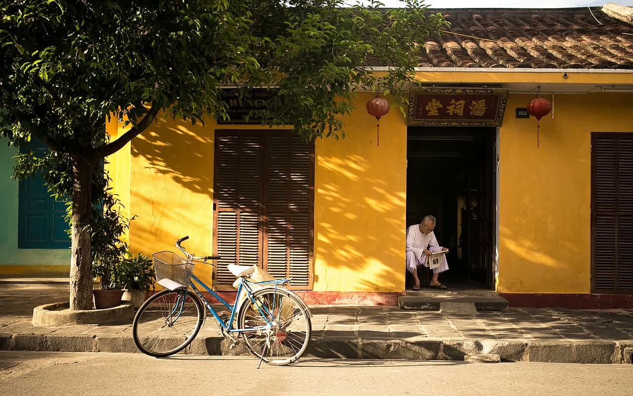 A bicycle leaning against a yellow house on a quiet Hoi An street