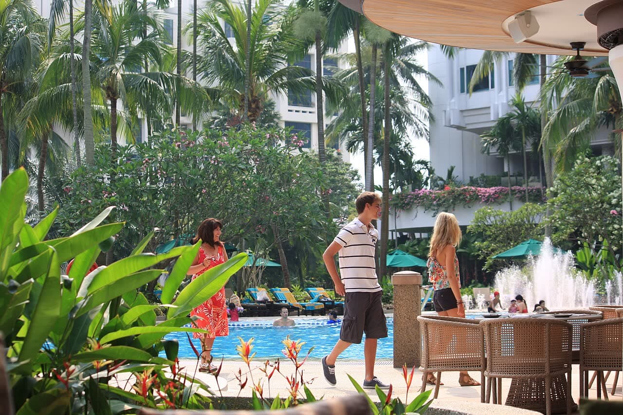 Guests walking through tropical gardens beside a resort pool at breakfast time